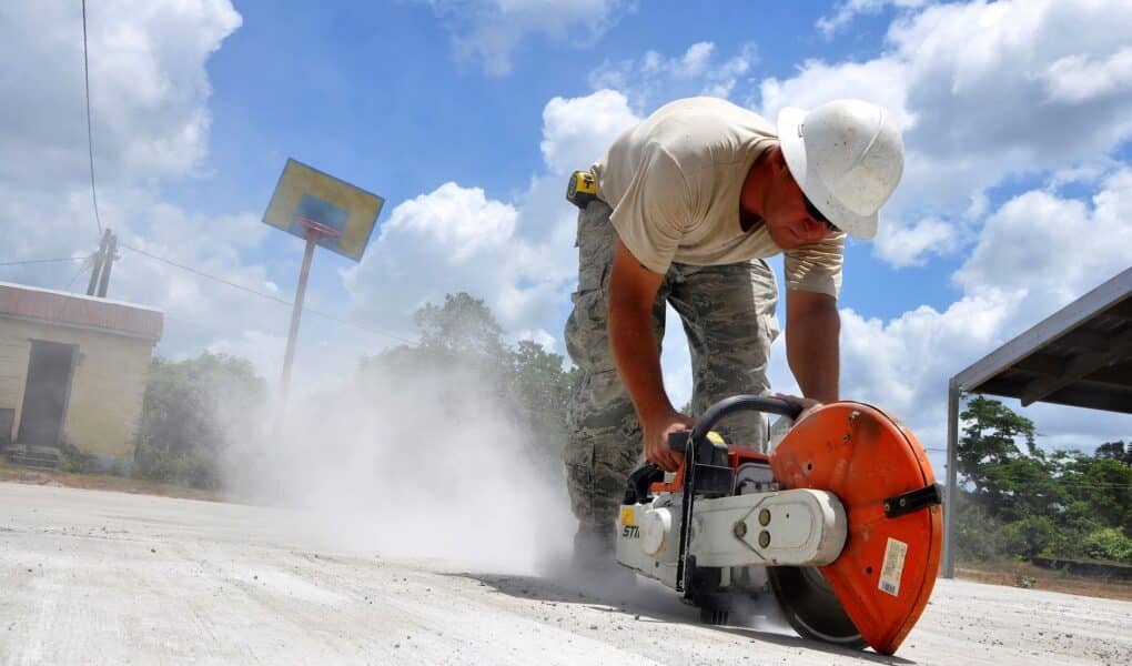 Ouvrier avec un casque qui est en train de découper une dalle béton avec une scie