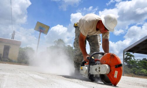 Ouvrier avec un casque qui est en train de découper une dalle béton avec une scie