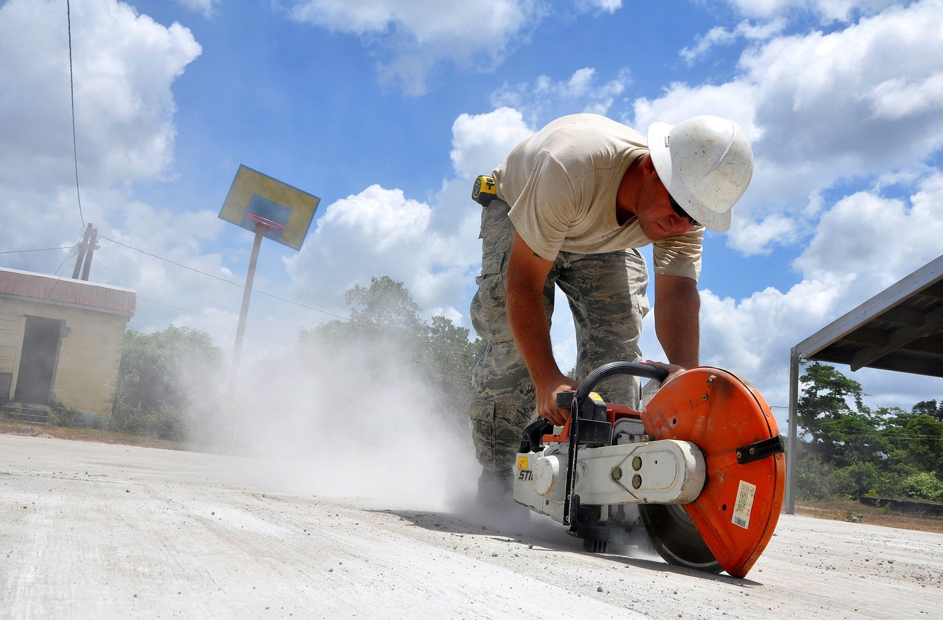 Ouvrier avec un casque qui est en train de découper une dalle béton avec une scie